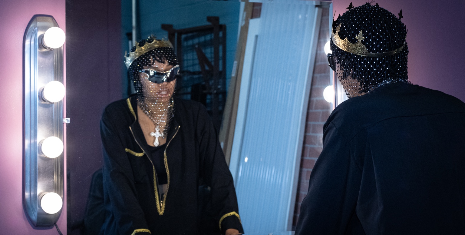 Indika Sam wearing a crown in front of a mirror